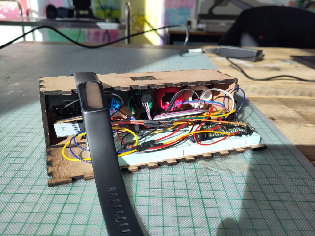 The finished product, a FitBit laying on a laser-cut wood box, containing electronics.